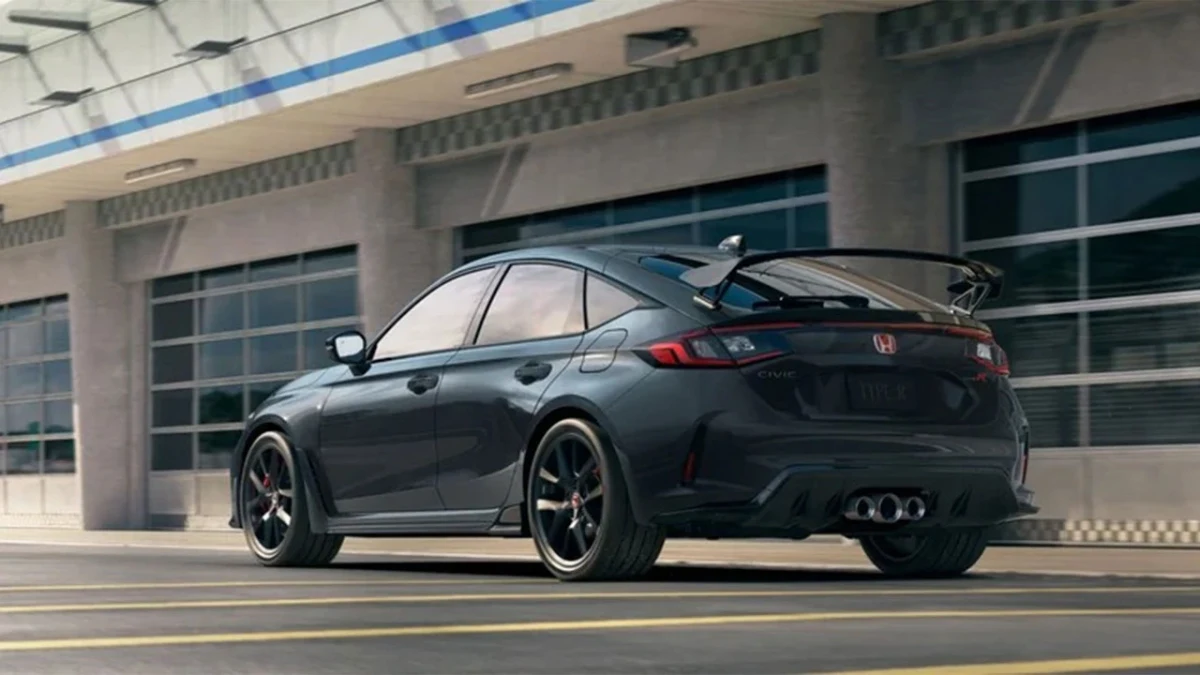 Koyu renkli Honda Civic Type R, modern bir binanın önünde arkadan üç çeyrek açıyla görüntüleniyor.