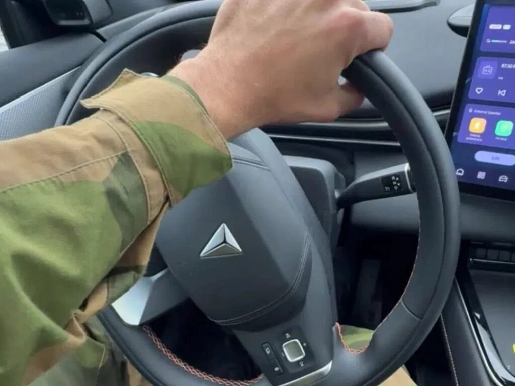 Askeri üniformalı bir kişinin otomobil direksiyonunu tuttuğu yakın plan