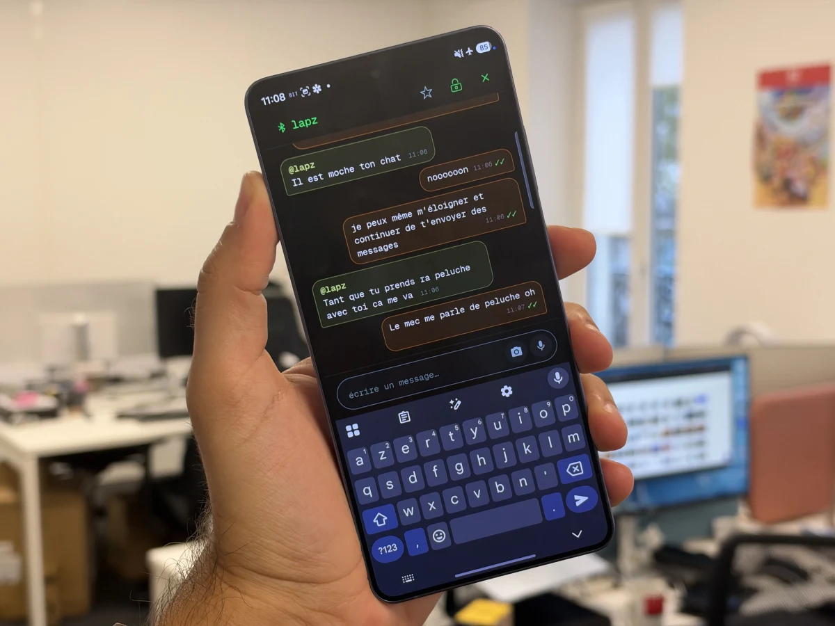 Bir kişinin elinde tuttuğu telefonda açık Bitchat mesajlaşma ekranı