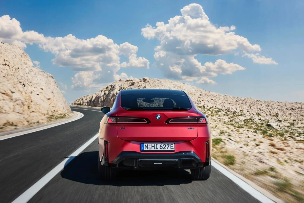Kırmızı BMW iX4 kıvrımlı yolda arkadan görüntüleniyor