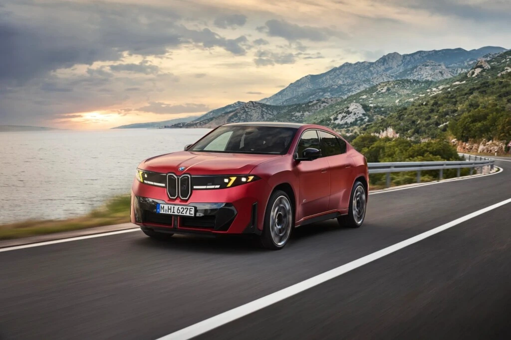 Kırmızı BMW iX4 dağlık kıyı yolunda ilerliyor