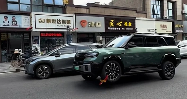 Ön tekerleğine sarı-kırmızı kilit takılmış yeşil BYD SUV, tekerleği havadayken caddede duruyor