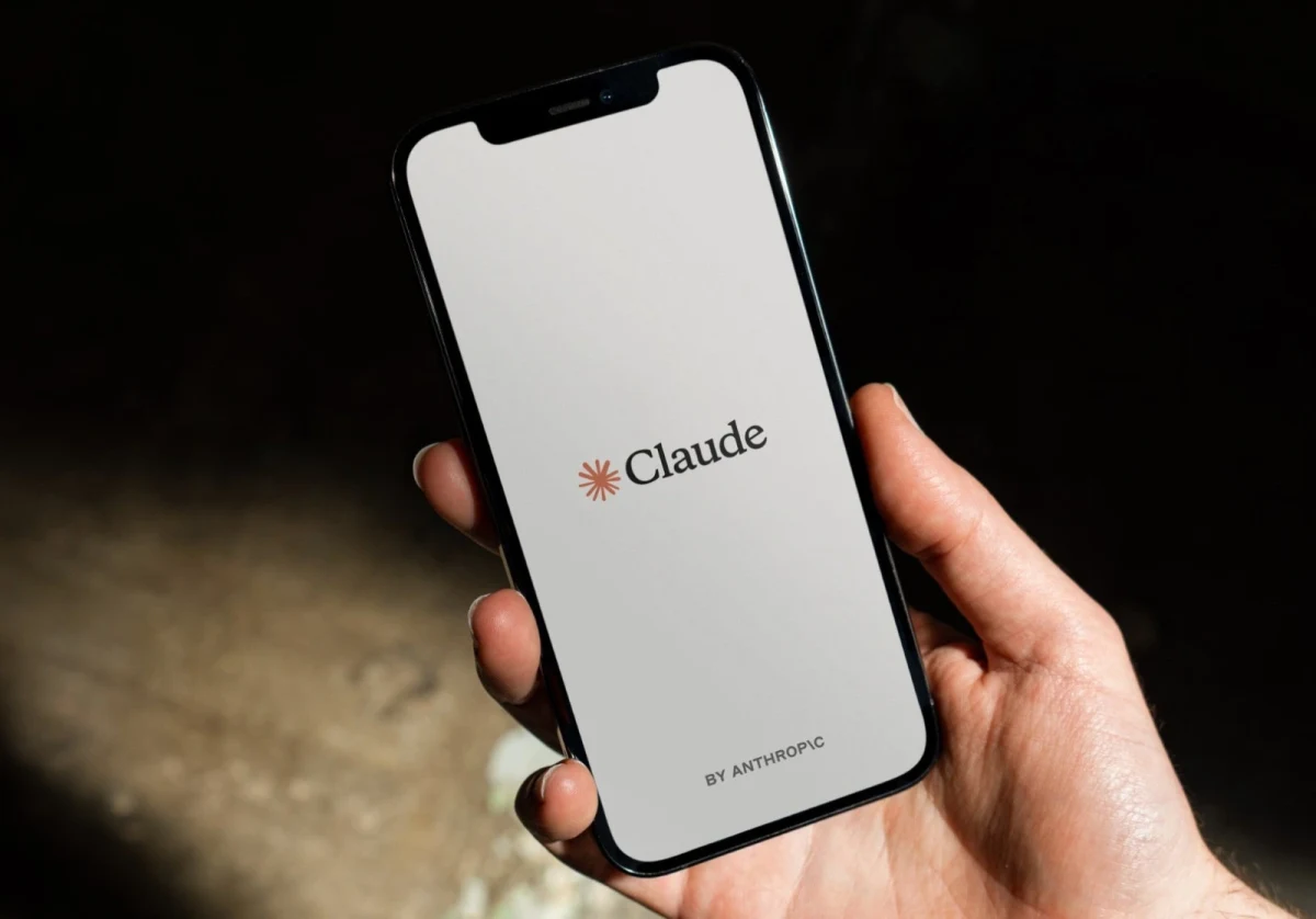 Bir kişinin elinde tuttuğu akıllı telefonun ekranında Claude logosu görülüyor.