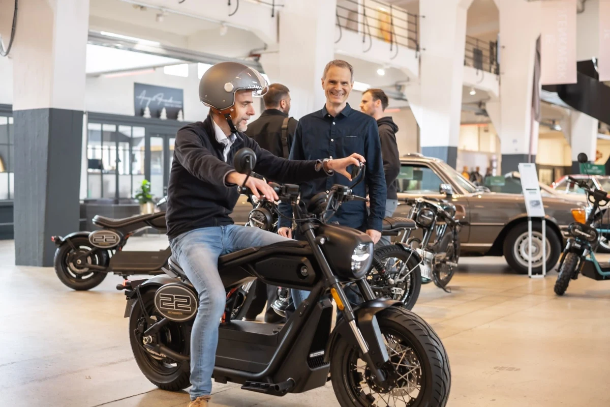 Bir kişinin Coopop Bobber motosiklet üzerinde, bir kişinin yanında durduğu motosiklet mağazası