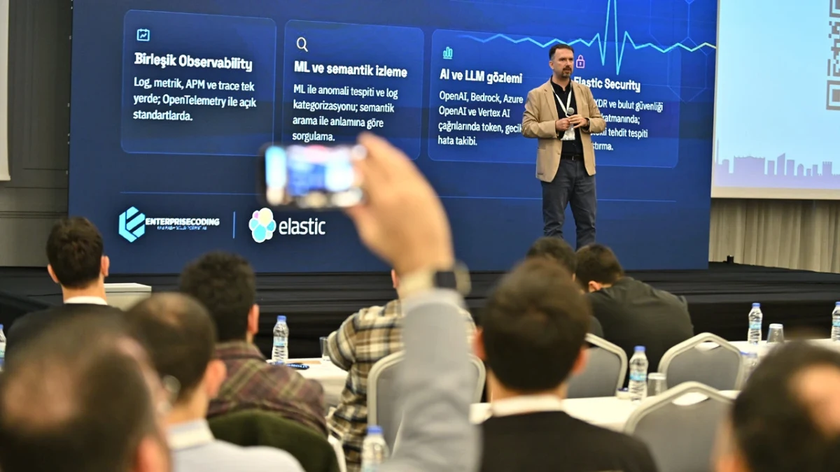 DevOpsDays İstanbul 2026’da bir konuşmacı sahnede sunum yaparken katılımcılardan biri telefonuyla görüntü alıyor