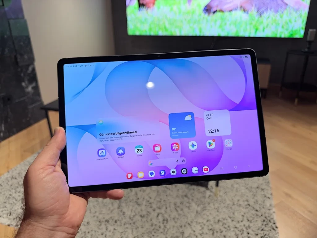 Elde tutulan Galaxy Tab ekranı ve arka plandaki televizyon