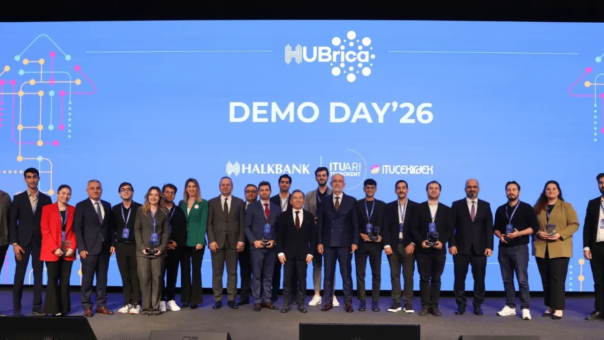 HUBrica Demo Day’26 sahnesinde etkinlik katılımcıları, arkalarında program logosunun ve Halkbank ile İTÜ Çekirdek logolarının bulunduğu mavi ekran önünde toplu halde duruyor.