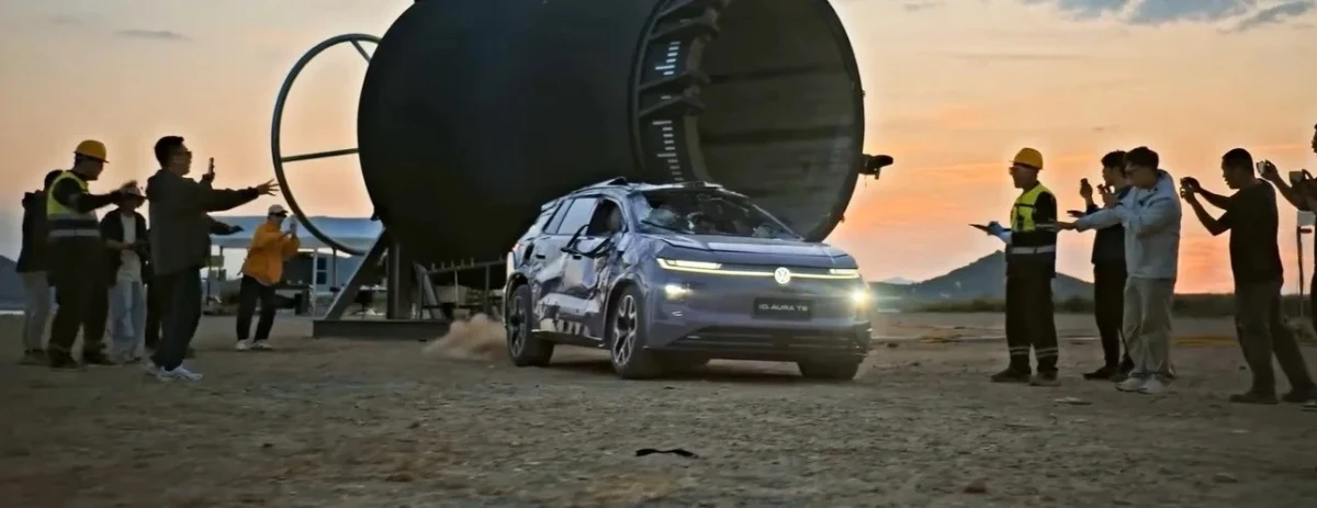 Hasar görmüş Volkswagen ID. AURA T6, büyük tamburun önünde dışarıda görüntüleniyor; çevrede izleyiciler bulunuyor.