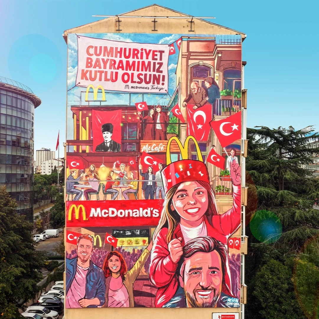 Cumhuriyet Bayramı mesajı ve Türk bayraklarıyla süslenmiş McDonald’s temalı bina illüstrasyonu