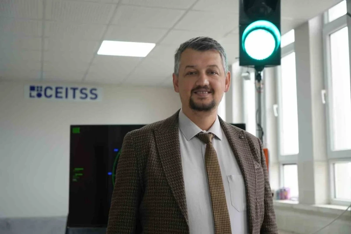 Kareli ceketli bir kişi, arkasında CEITSS yazısı ve yeşil ışıklı cihazla kapalı bir alanda duruyor