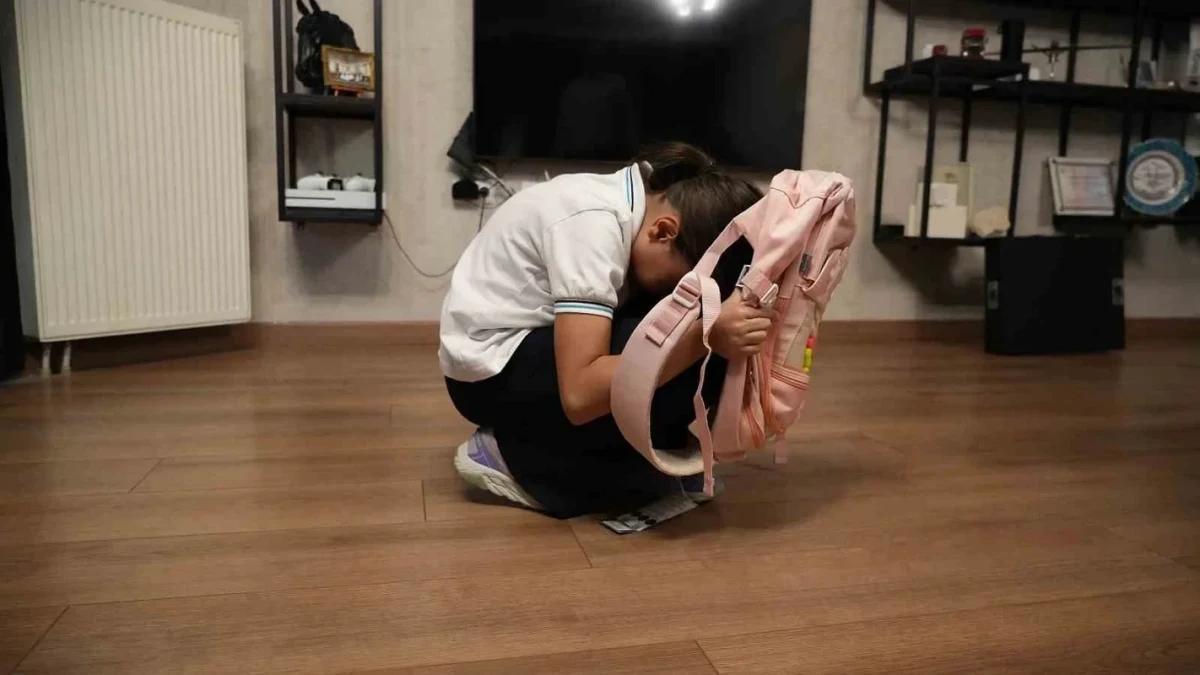 Bir öğrenci pembe okul çantasını önünde tutarak çömeliyor