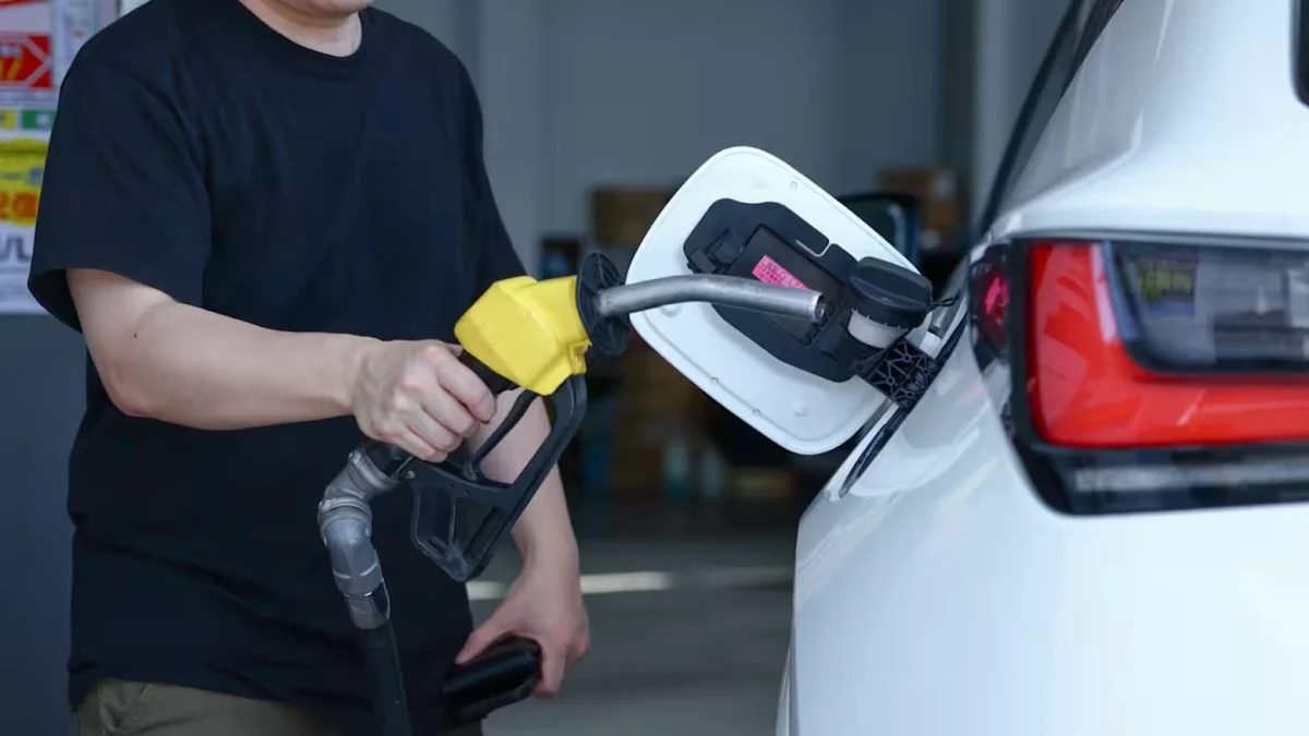 Bir kişi benzin pompasını beyaz bir otomobilin yakıt deposuna takıyor