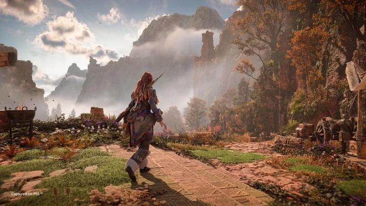 Horizon Forbidden West’te Aloy, dağlık ve bitki örtüsüyle kaplı bir arazide ilerliyor.