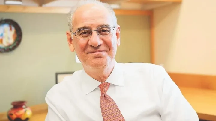 Prof. Dr. Rıfat Atun, beyaz gömlek ve desenli kravatla otururken