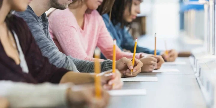Sınav salonunda masalarda yazı yazan öğrenciler