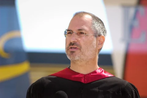 Steve Jobs, siyah cübbe ve kırmızı yakayla bir etkinlikte konuşurken