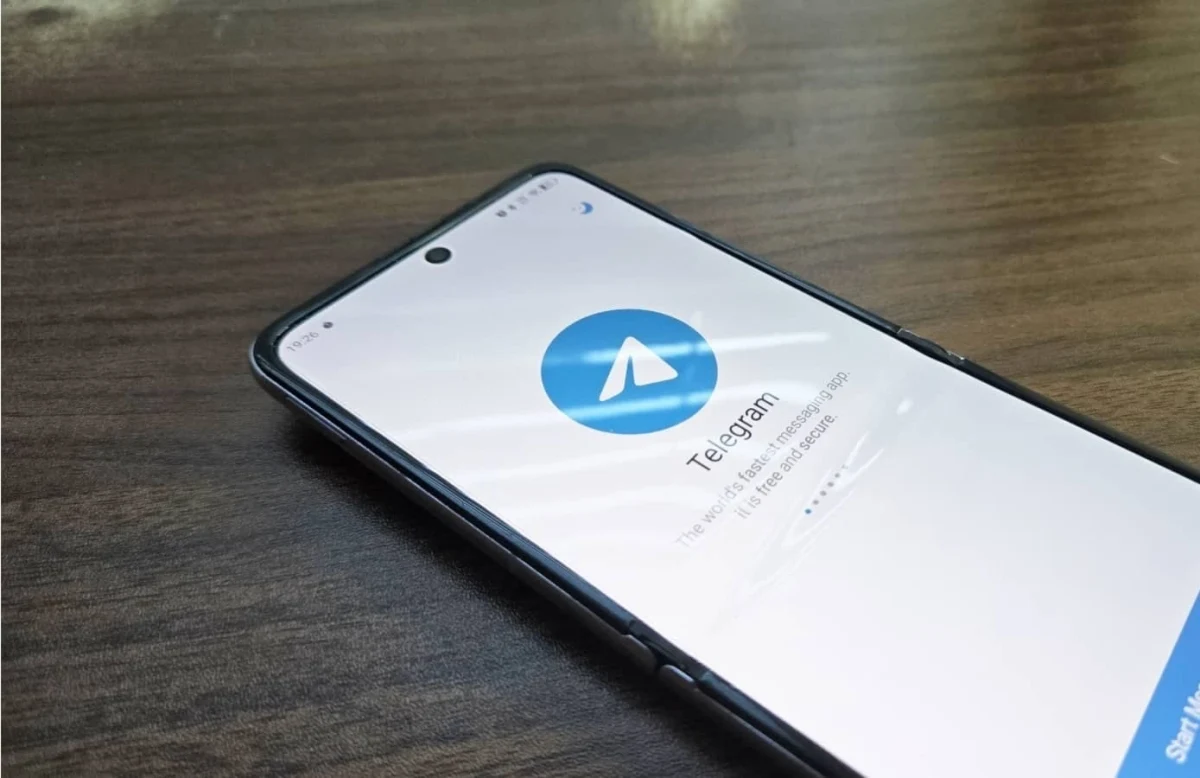 Telegram uygulamasının açık olduğu bir akıllı telefon ahşap yüzeyde duruyor