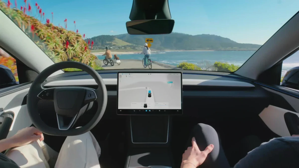 Tesla araç içinden, ön konsol ve orta ekrana doğru görünen sahil yolu manzarası