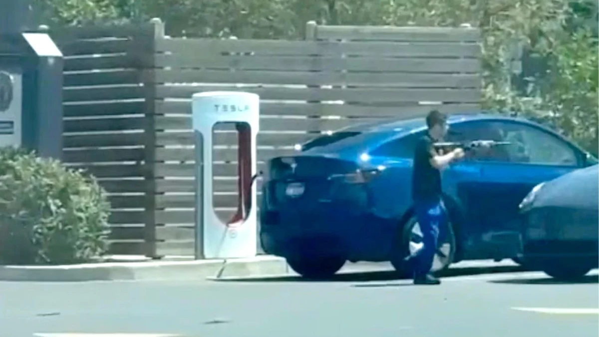 Tesla şarj istasyonunun yanında duran mavi otomobil ve bir kişi
