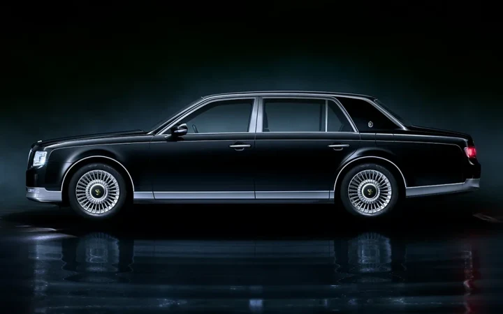 Koyu renkli Toyota Century sedan, yandan görünümüyle karanlık bir stüdyo ortamında sergileniyor.