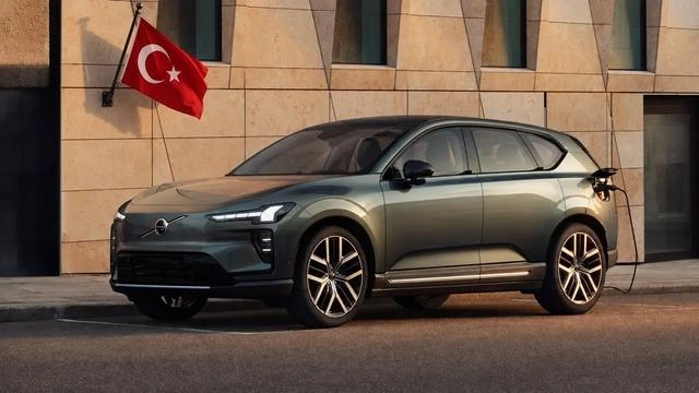 Bir binanın önünde park etmiş gri Volvo EX60 ve aracın arkasında Türkiye bayrağı