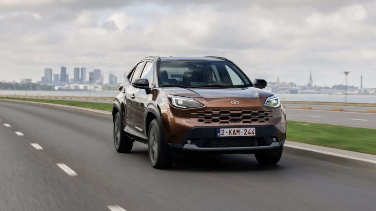 Kahverengi Toyota Yaris Cross Hybrid, yolda ilerlerken önden görüntüleniyor.